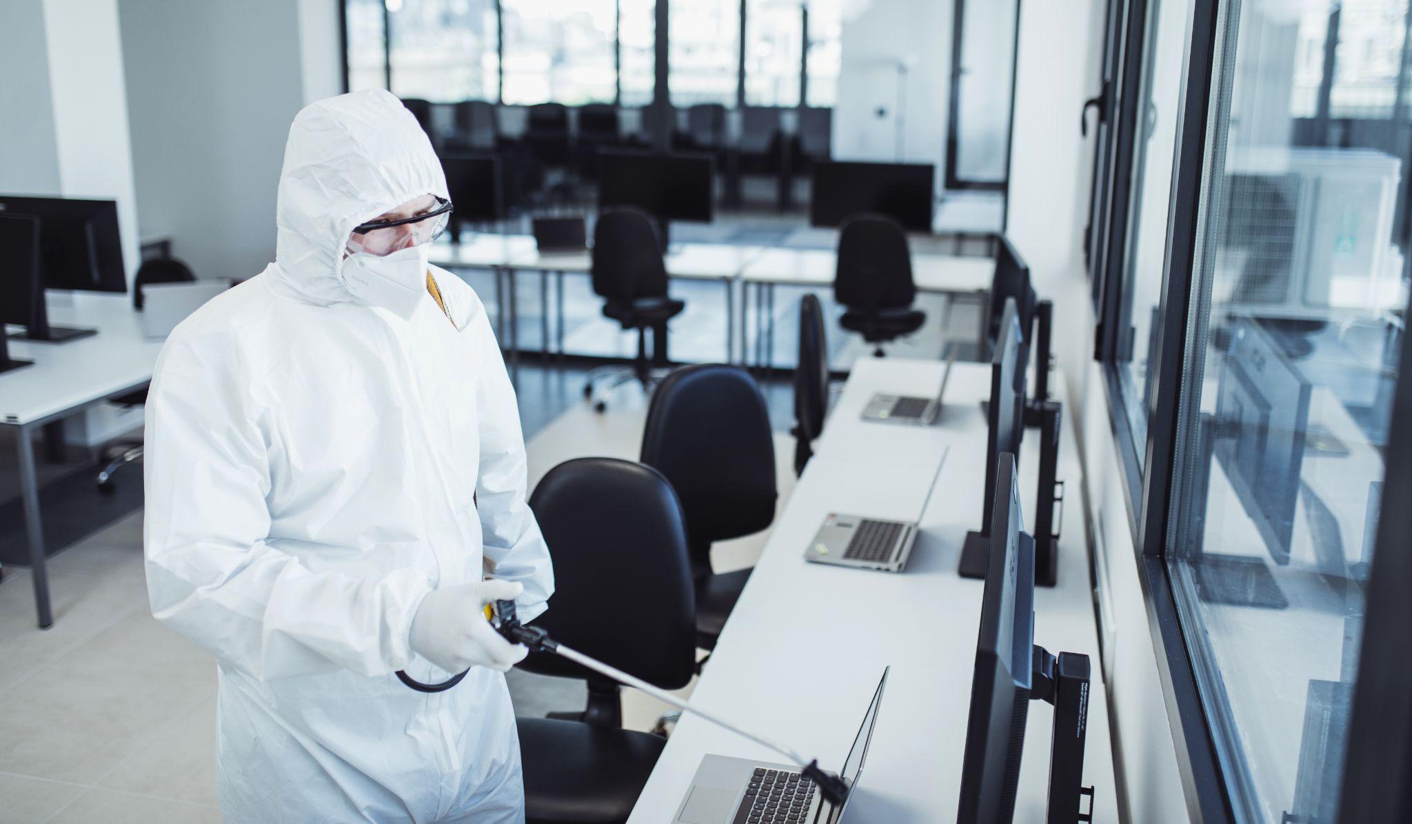 Man in protective suit and face mask spraying for disinfection in the office