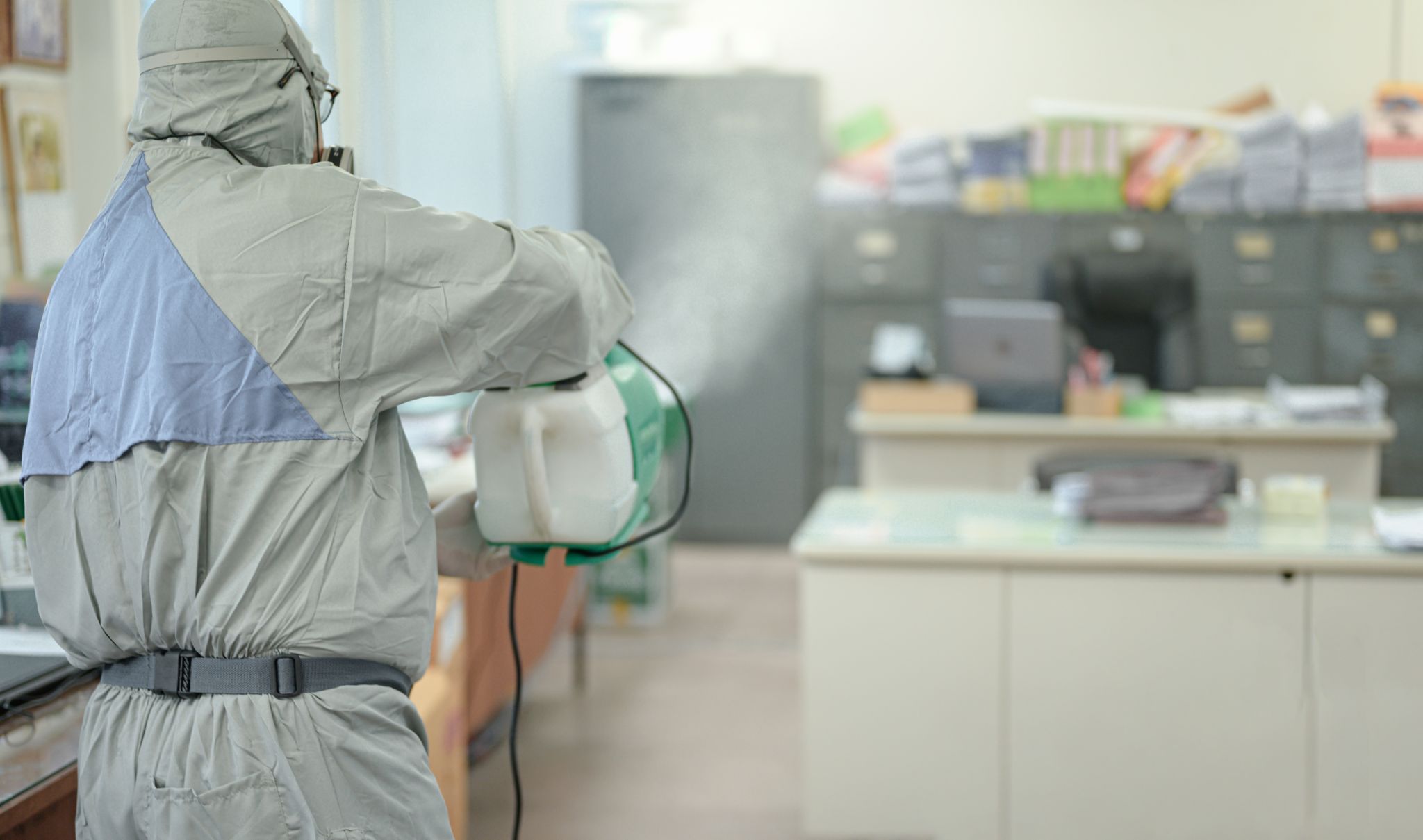 person in white hazmat suit with disinfect in office