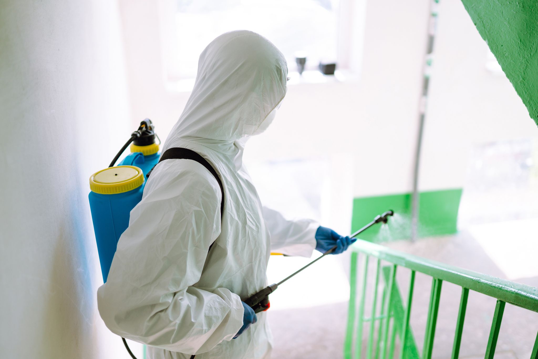 Sanitary professional worker wearing hazmat suit disinfects a staircase entryway block of flats.