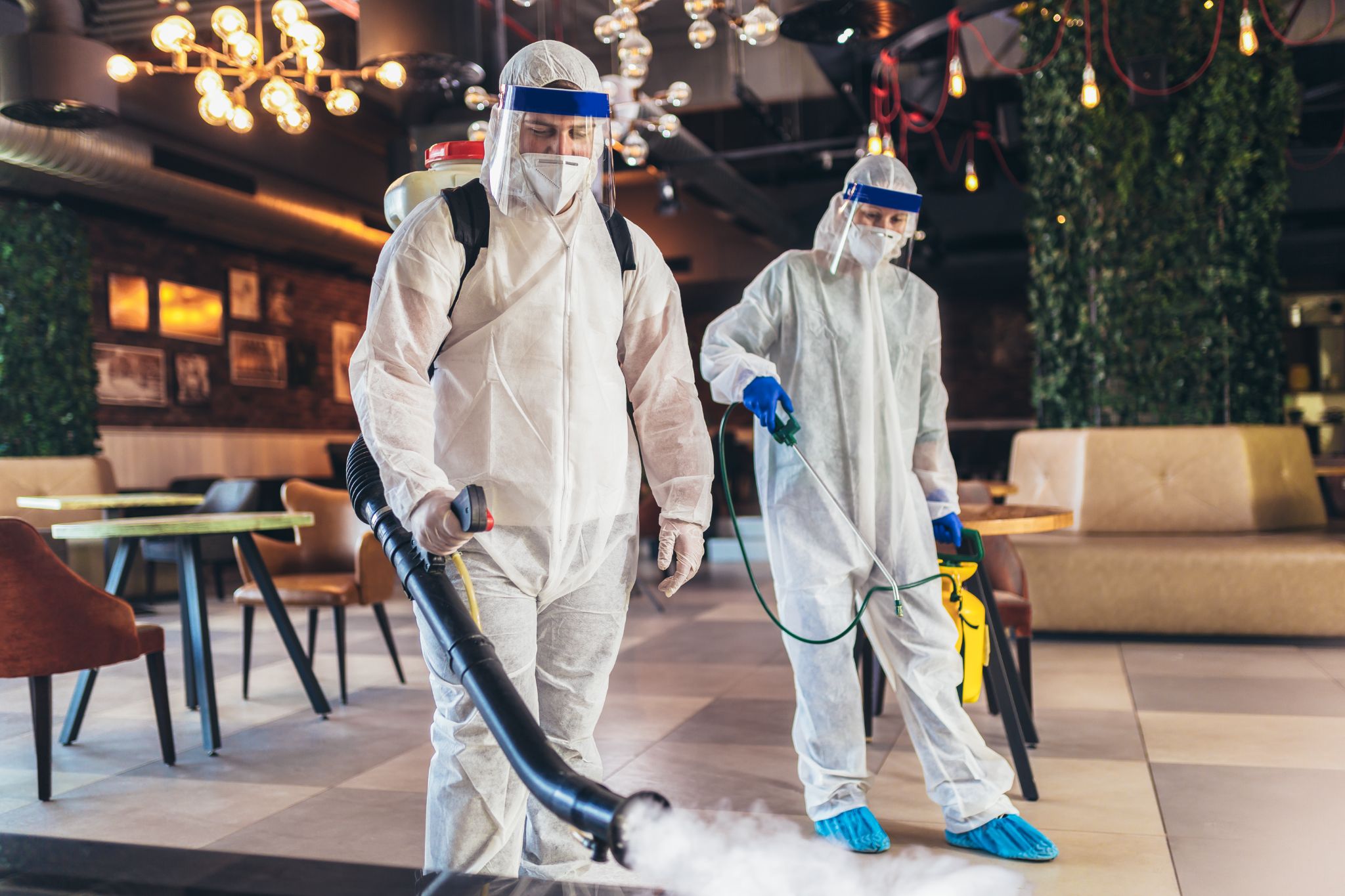 Professional workers in hazmat suits disinfecting indoor of cafe or restaurant