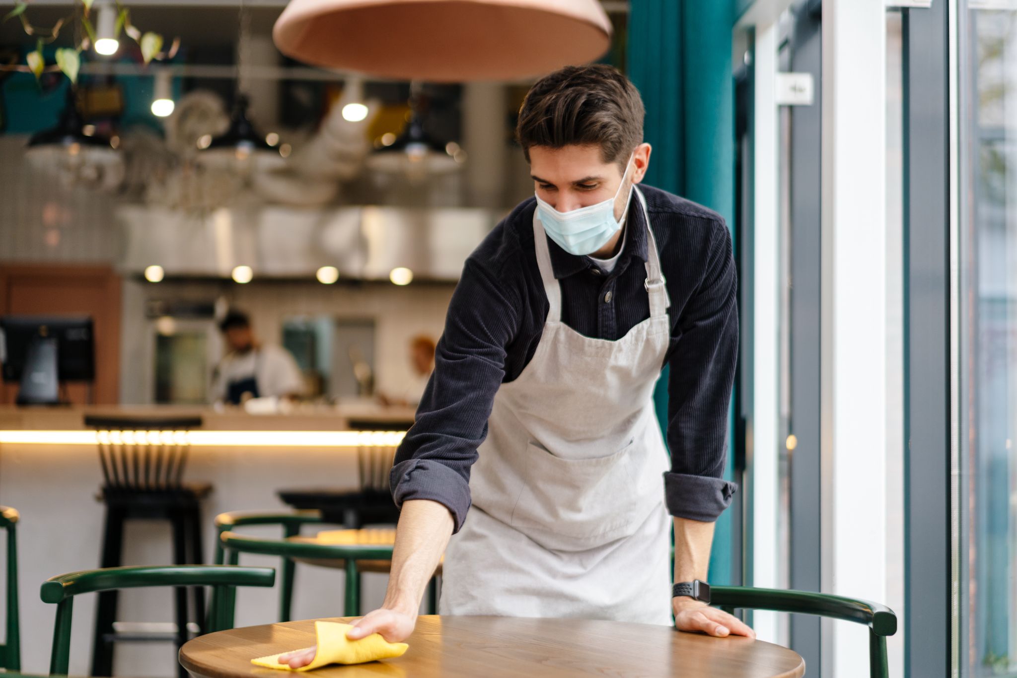 waiter wearing mask disinfecting table in the cafe