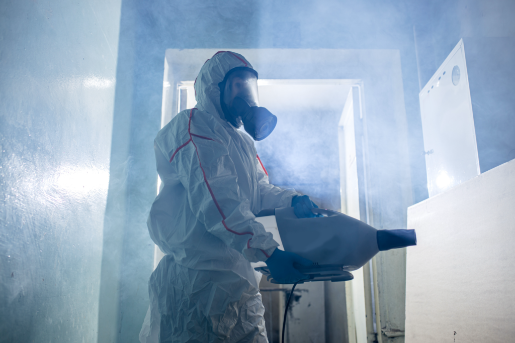 Professional disinfector in protective suit indoors, kill and remove bacterias from surfaces