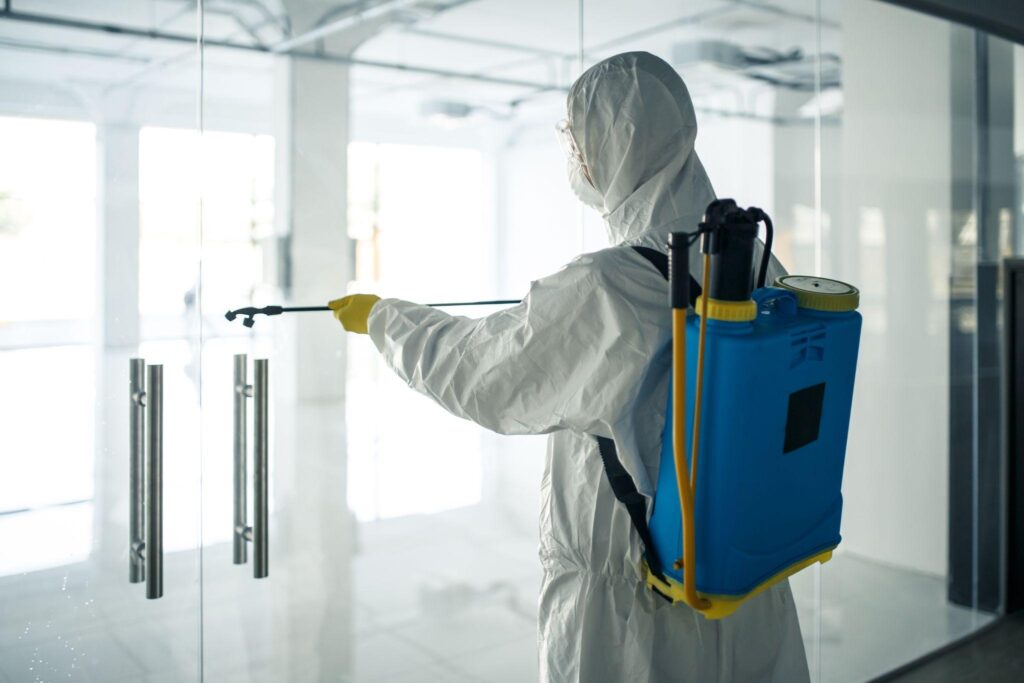 A man sanitizer the glass doors' handles in an empty shopping mall to prevent covid-19 spread.